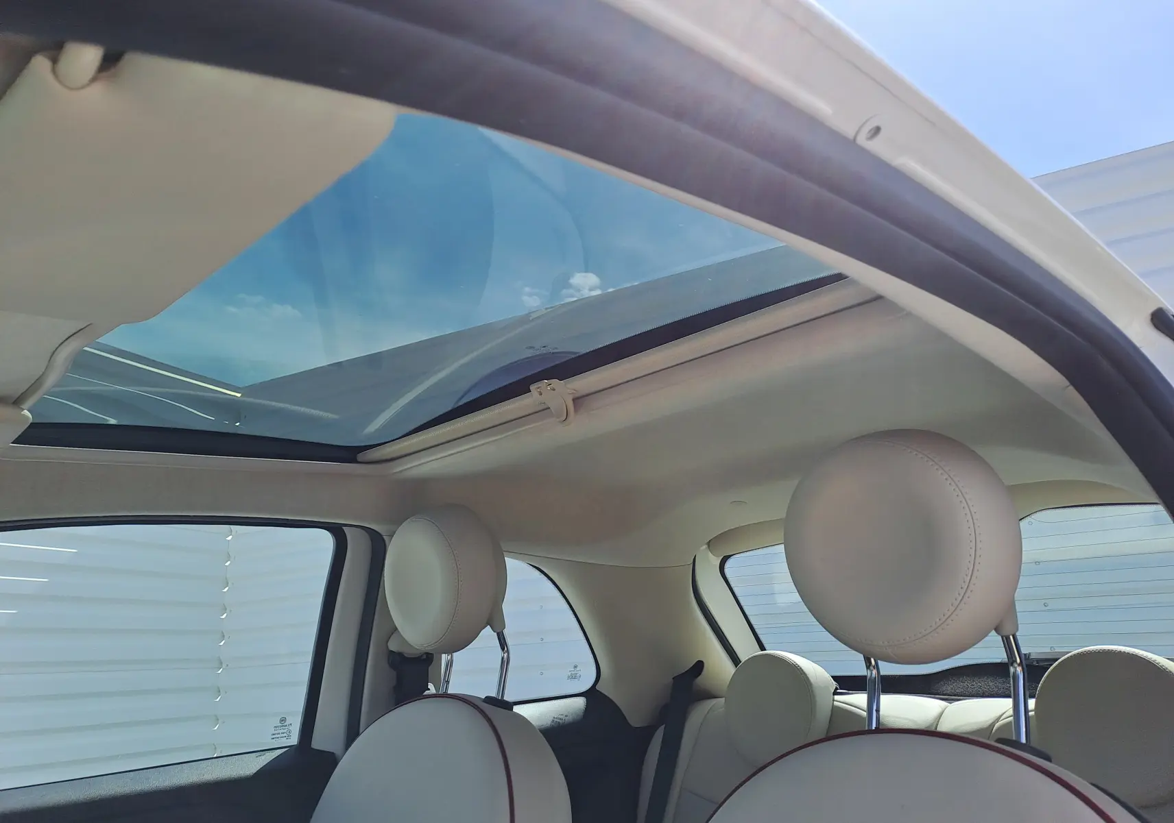 Intérieur blanc crème de la Fiat 500 1.0 Hybrid 2022 avec toit panoramique ouvrant et sièges avant arrondis.