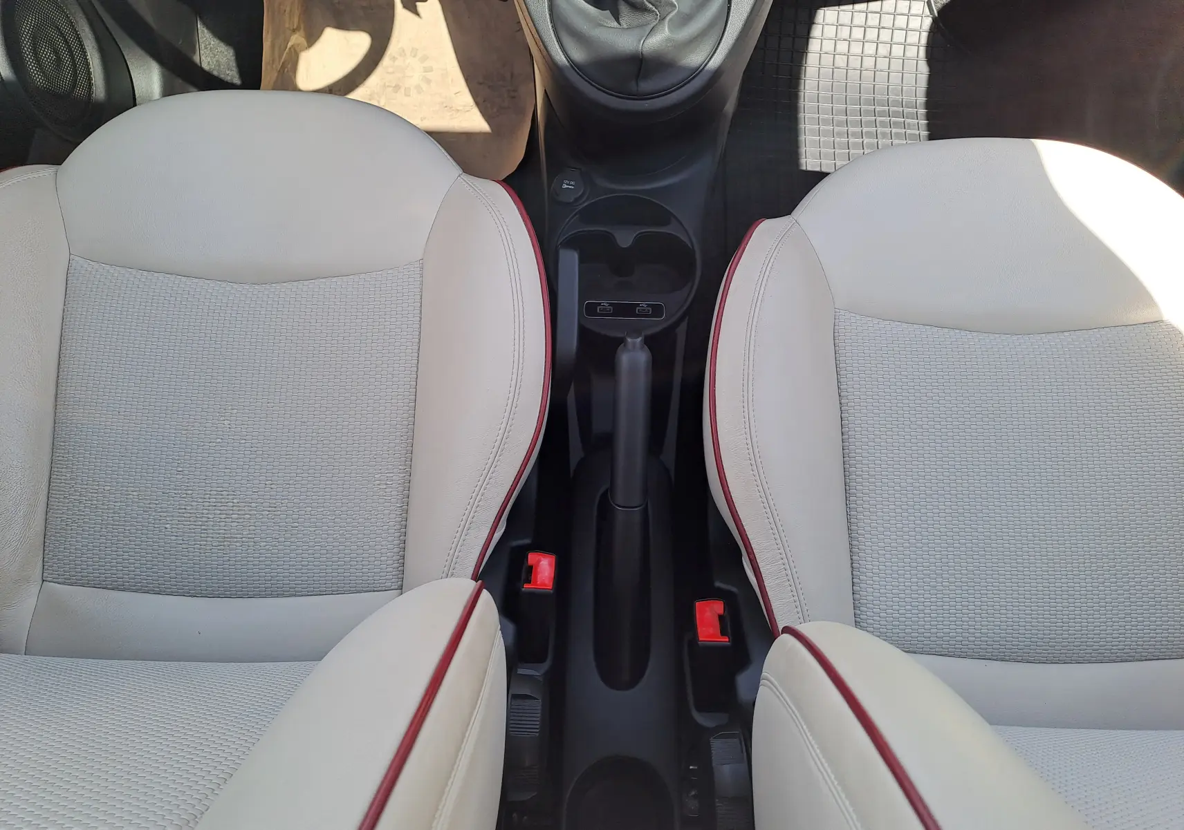 Vue plongeante sur les sièges avant beige clair avec surpiqûres rouges et levier de frein à main central d'une Fiat 500 blanche.