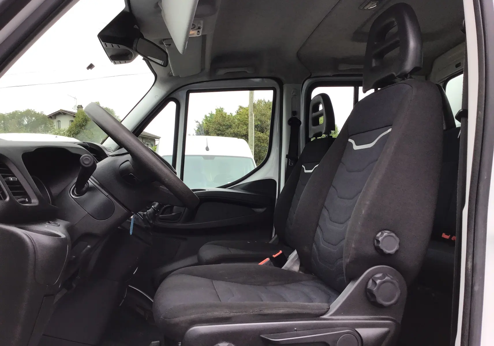 Vue intérieure côté conducteur de l'Iveco Daily blanc 2021, montrant les sièges noirs et le volant multifonction.