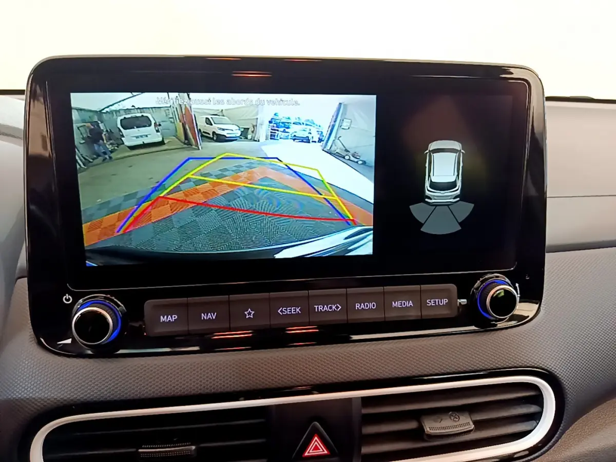 Écran tactile central du Hyundai Kona noir 2020 montrant l'aide au stationnement arrière avec caméra et capteurs.