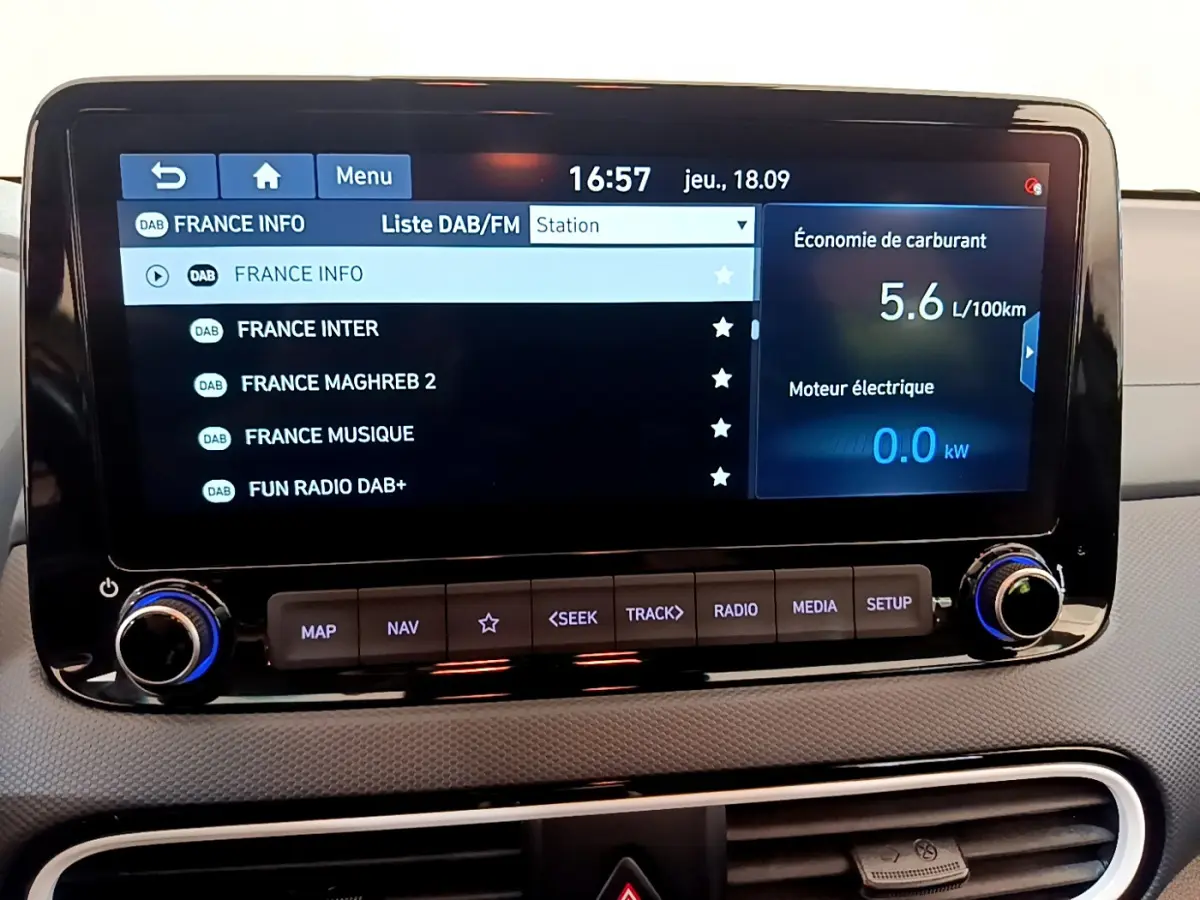 Écran tactile central du tableau de bord du Hyundai Kona noir, affichant la liste des radios DAB et consommation hybride.