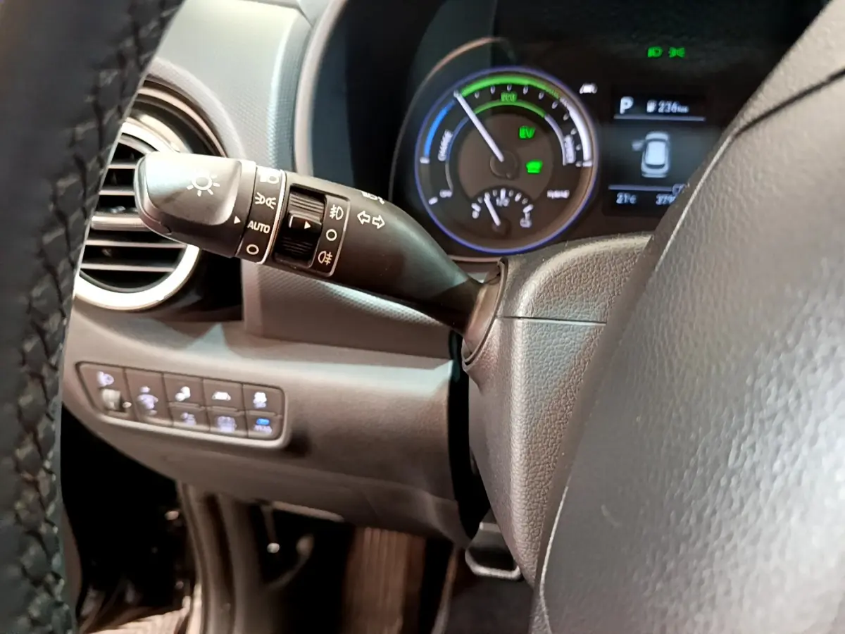 Gros plan sur la manette de feux à gauche du volant cuir du Hyundai Kona hybride noir, avec tableau de bord numérique en arrière-plan.