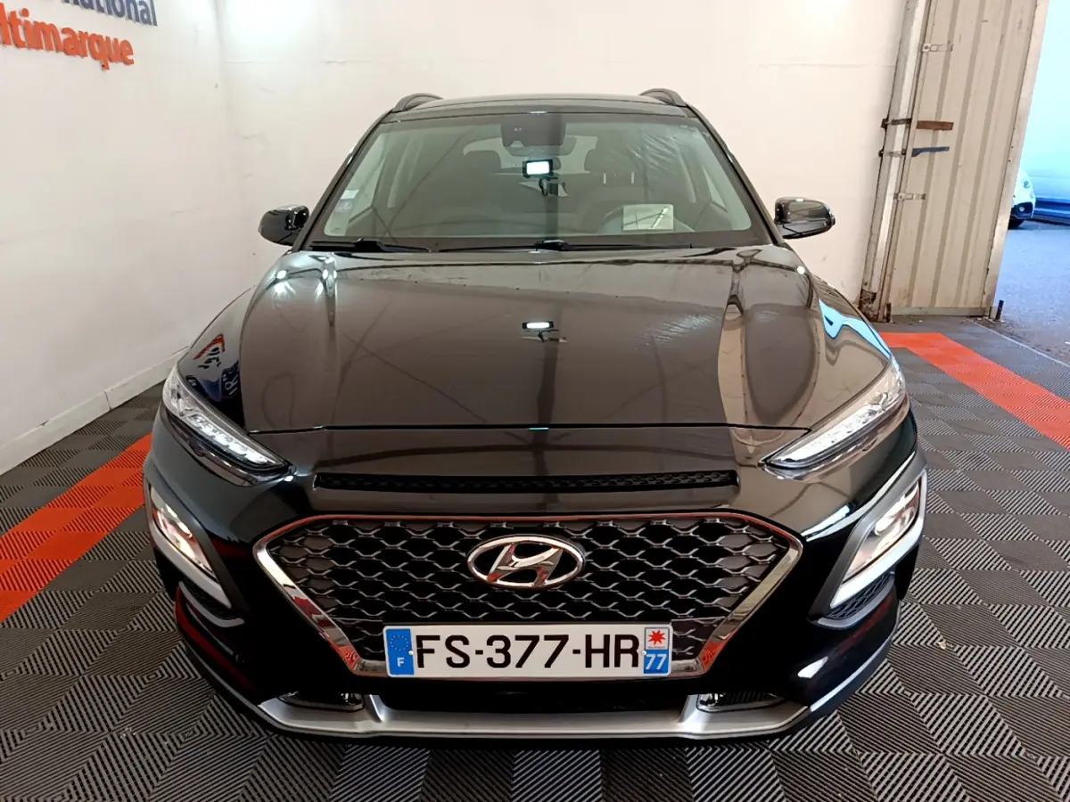 Vue avant d'un Hyundai Kona noir 2020 avec calandre hexagonale et feux LED, stationné en intérieur sur sol à motifs.