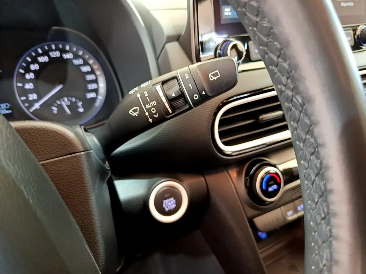 Gros plan intérieur sur le volant noir et la commande essuie-glace du Hyundai Kona hybride 2020 avec bouton démarrage.