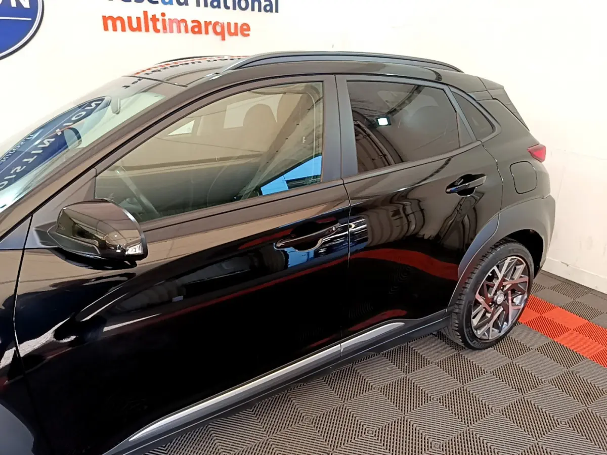 Vue latérale côté gauche d'un Hyundai Kona noir brillant avec jantes alliage et rétroviseurs noirs dans un showroom.