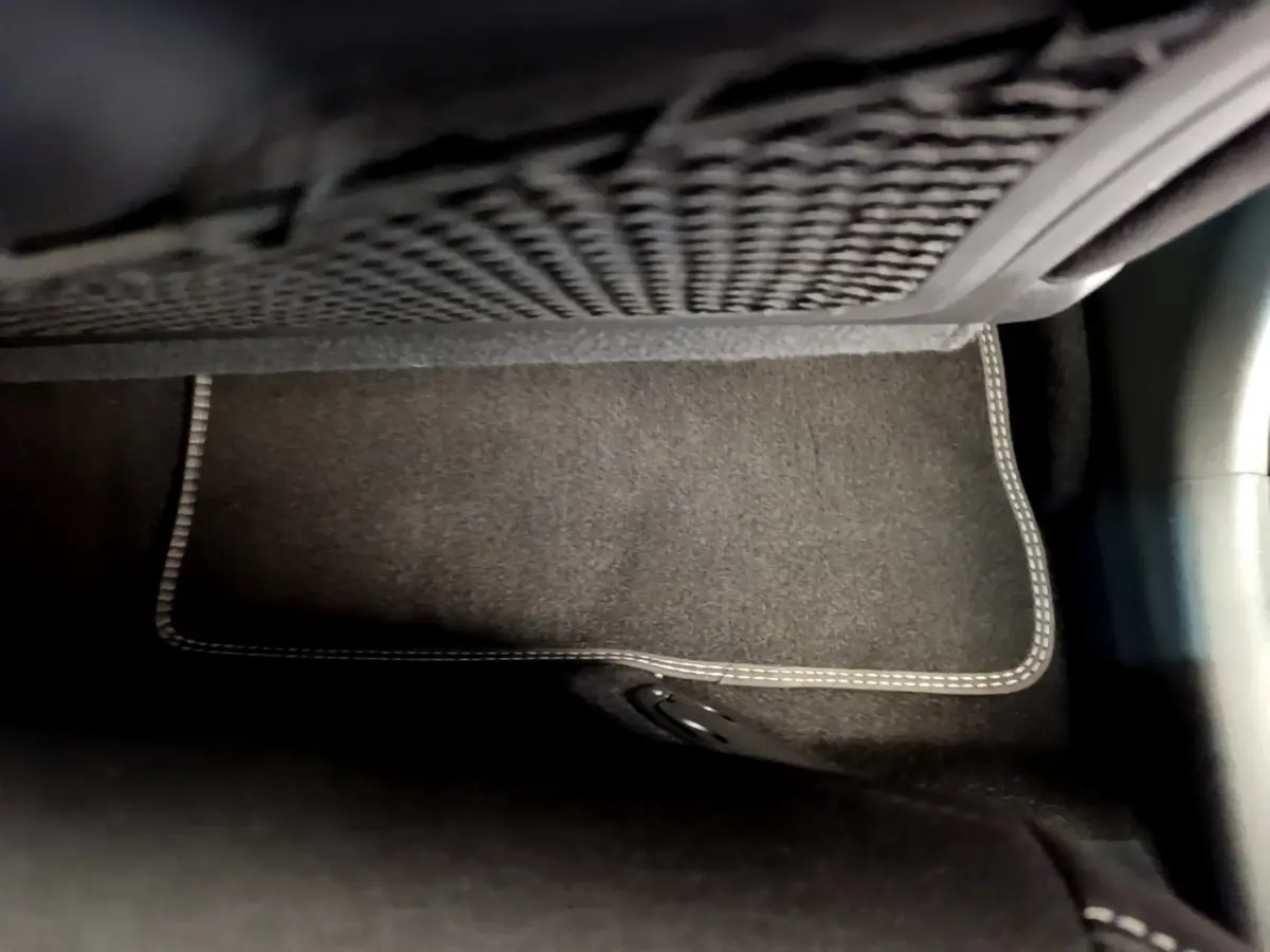 Tapis de sol noir avec surpiqûres blanches sous le filet de rangement, intérieur d’un Hyundai Kona hybride 2020.