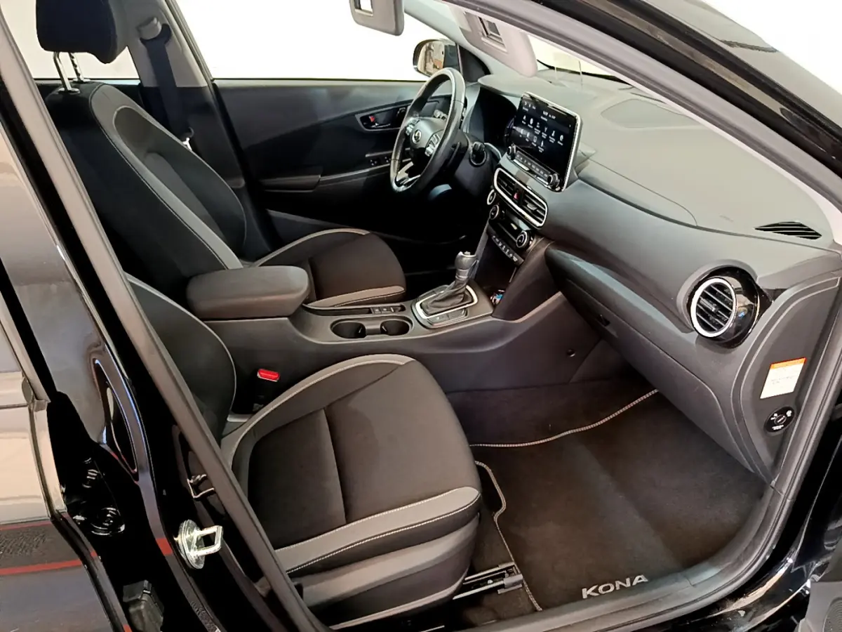 Intérieur côté conducteur d'une Hyundai Kona noire, montrant sièges noirs, volant cuir et écran tactile central.