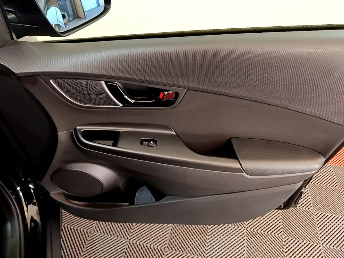 Intérieur côté gauche de la porte avant d'un Hyundai Kona noir, avec poignée chromée et commande de vitre électrique.