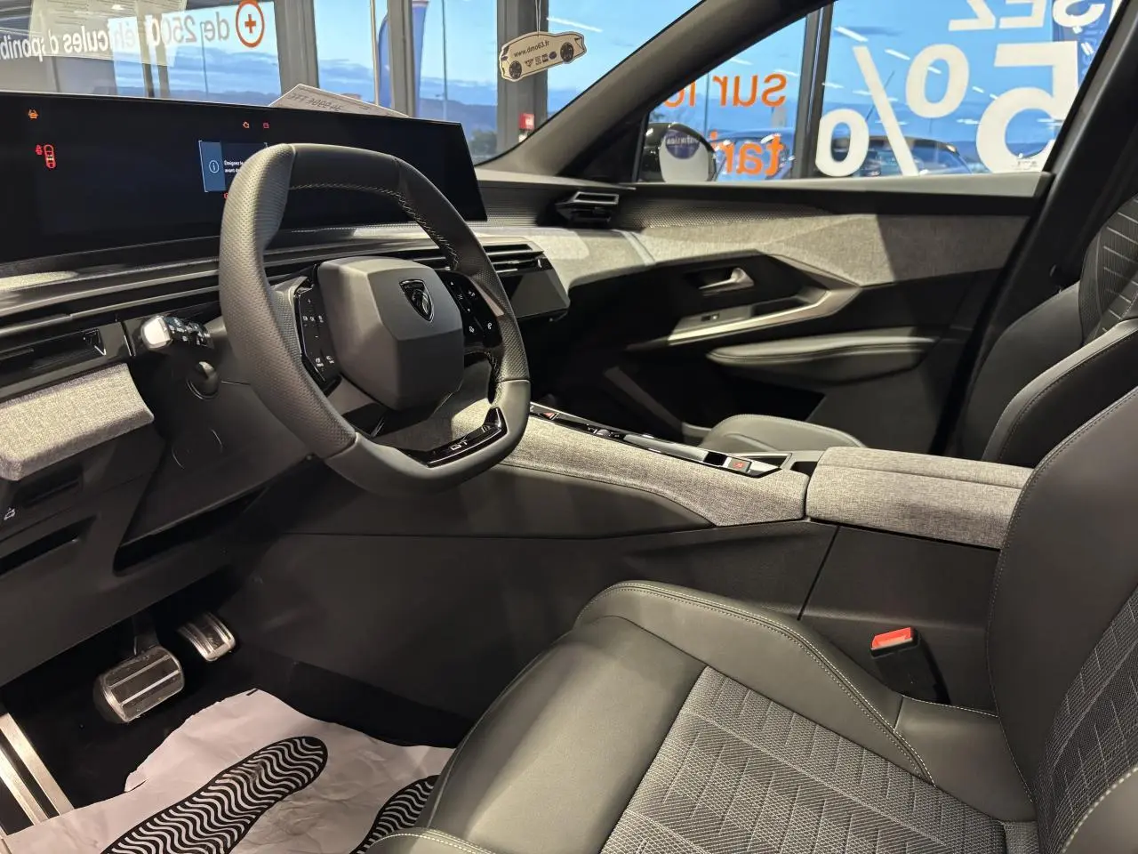 Intérieur avant droit du Peugeot 3008 Hybrid 2025, avec volant compact, sellerie tissu gris et décor tissu Rimini chiné.