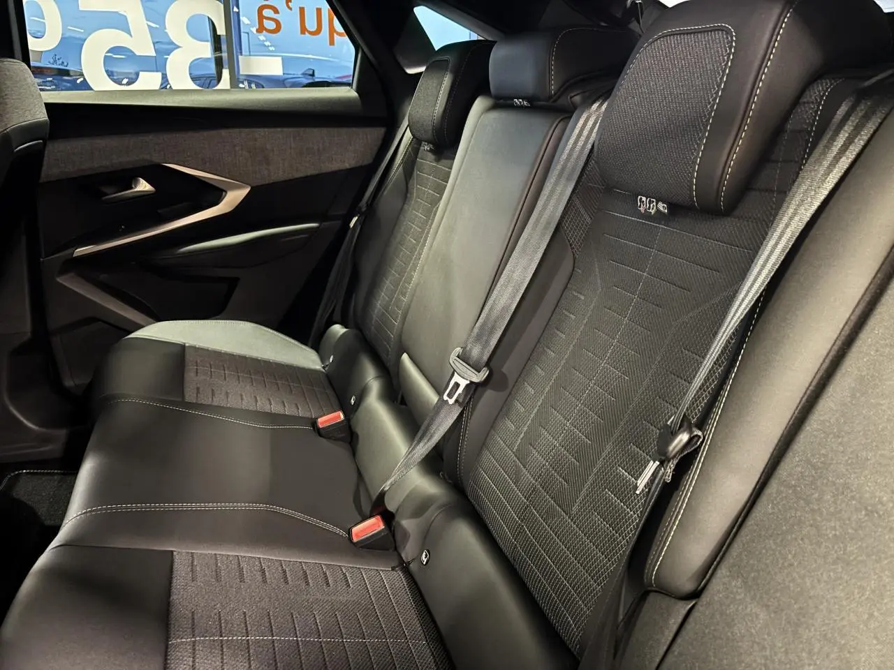 Vue côté droit de la banquette arrière en tissu et cuir noir du Peugeot 3008 Hybrid 2025 avec ceinture de sécurité attachée.