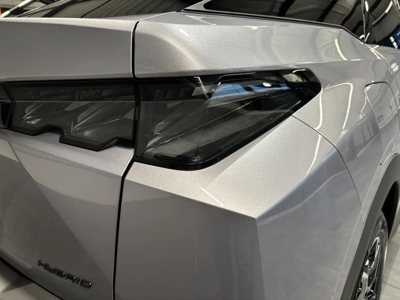 Gros plan sur le feu arrière droit du Peugeot 3008 gris Artense avec bandeau noir laqué et monogramme Hybrid.