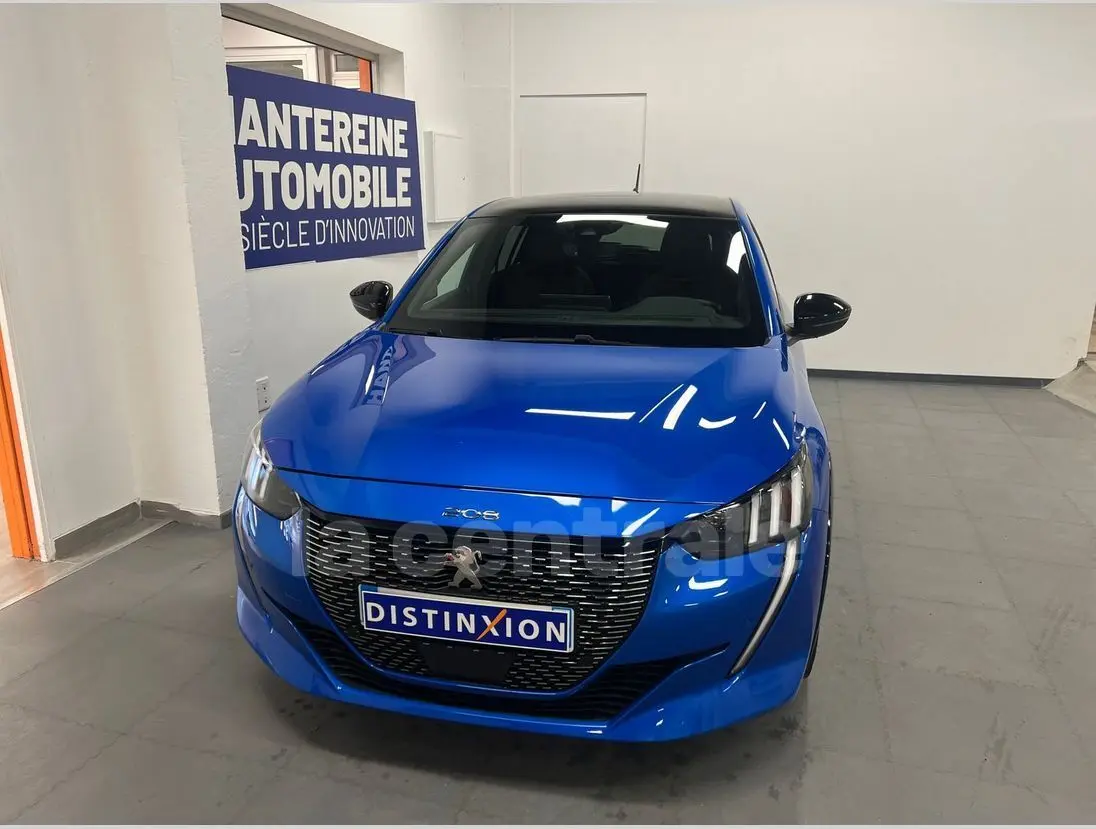 Peugeot 208 bleu en 3/4 avant, avec calandre noire distinctive et phares LED, vue dans un showroom intérieur.