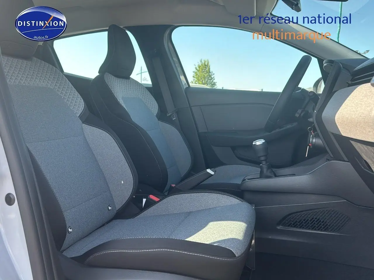 Intérieur de la Renault Clio 2025 vu côté gauche, sièges tissu gris à motifs et levier de vitesse manuel visible.