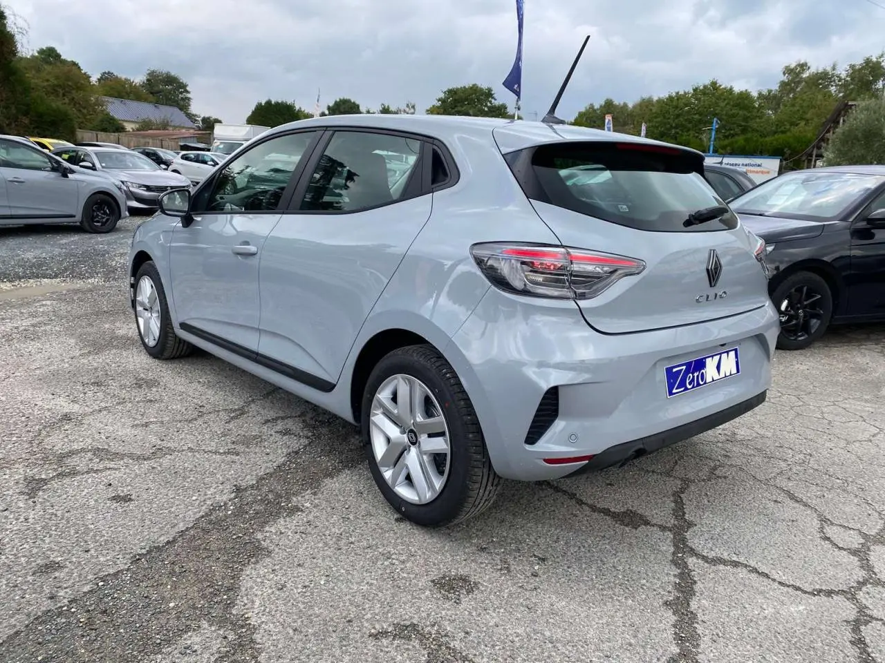 Renault Clio 2025 gris Rafale vue 3/4 arrière droit, avec feux LED et jantes alliage visibles sur parking.