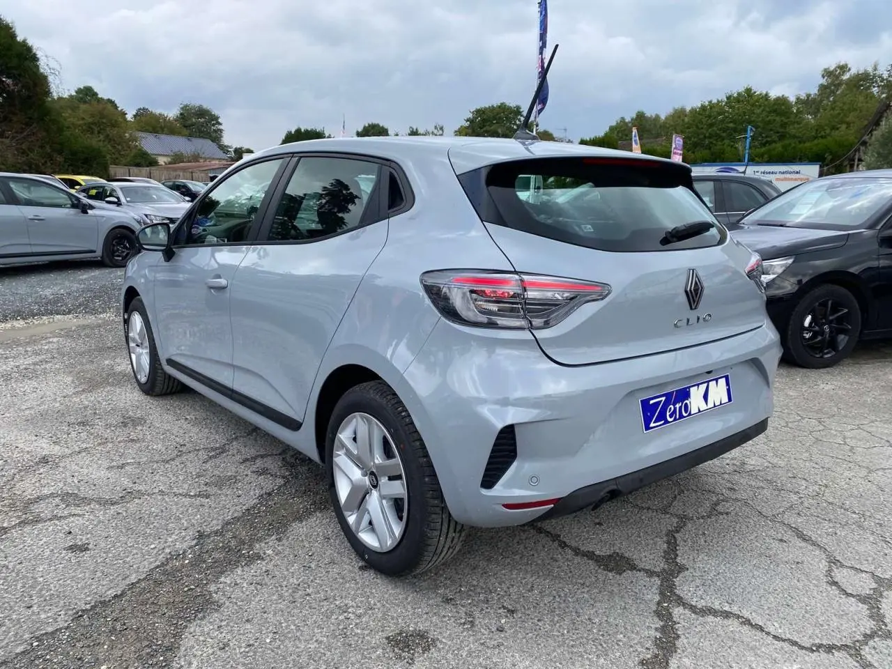 Renault Clio 2025 gris Rafale vue 3/4 arrière droit, avec feux LED et jantes alliage visibles sur parking.