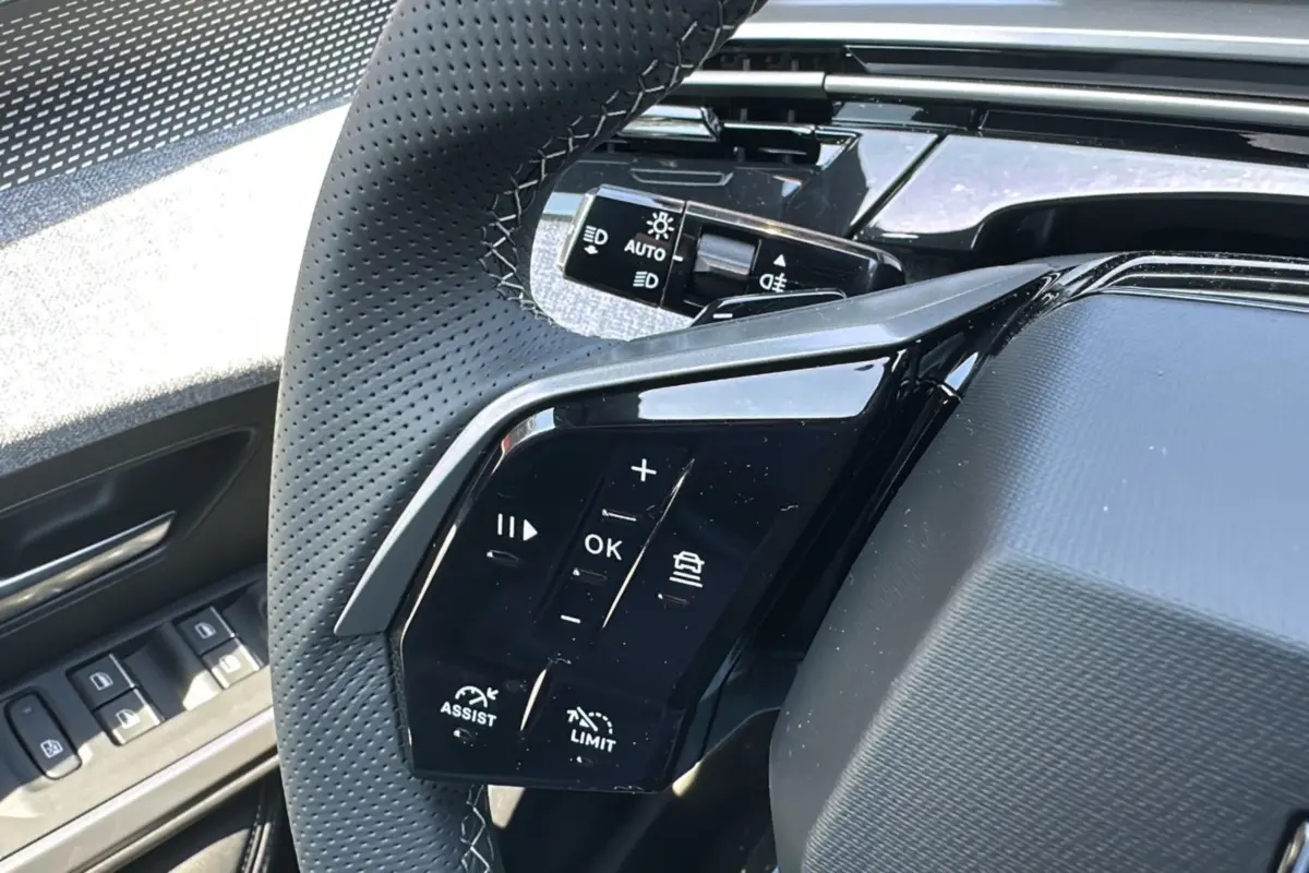 Gros plan sur les commandes au volant du Peugeot 3008 hybride 2025 avec finition noire brillante et cuir perforé.