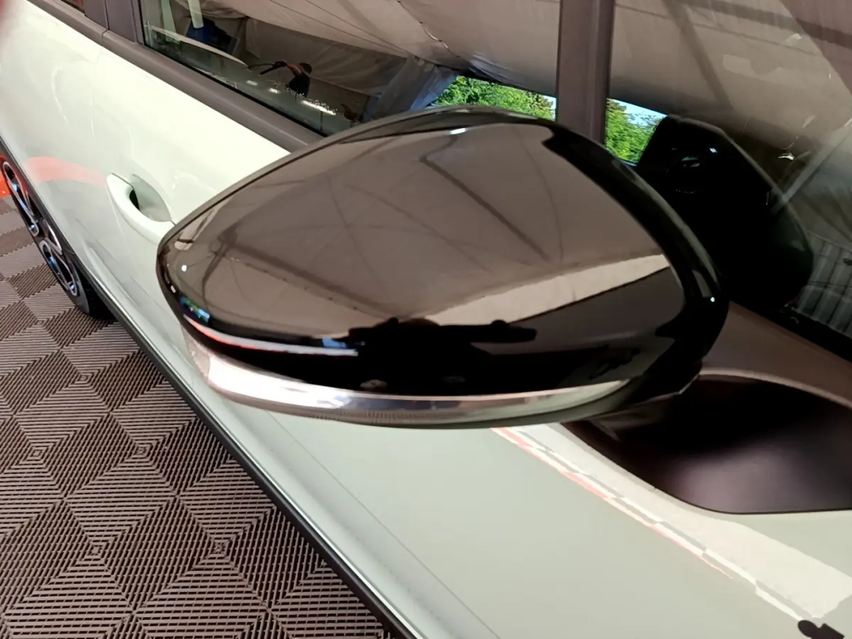 Gros plan sur le rétroviseur noir brillant côté gauche d'une Citroën C3 vert clair, avec poignée de porte visible.