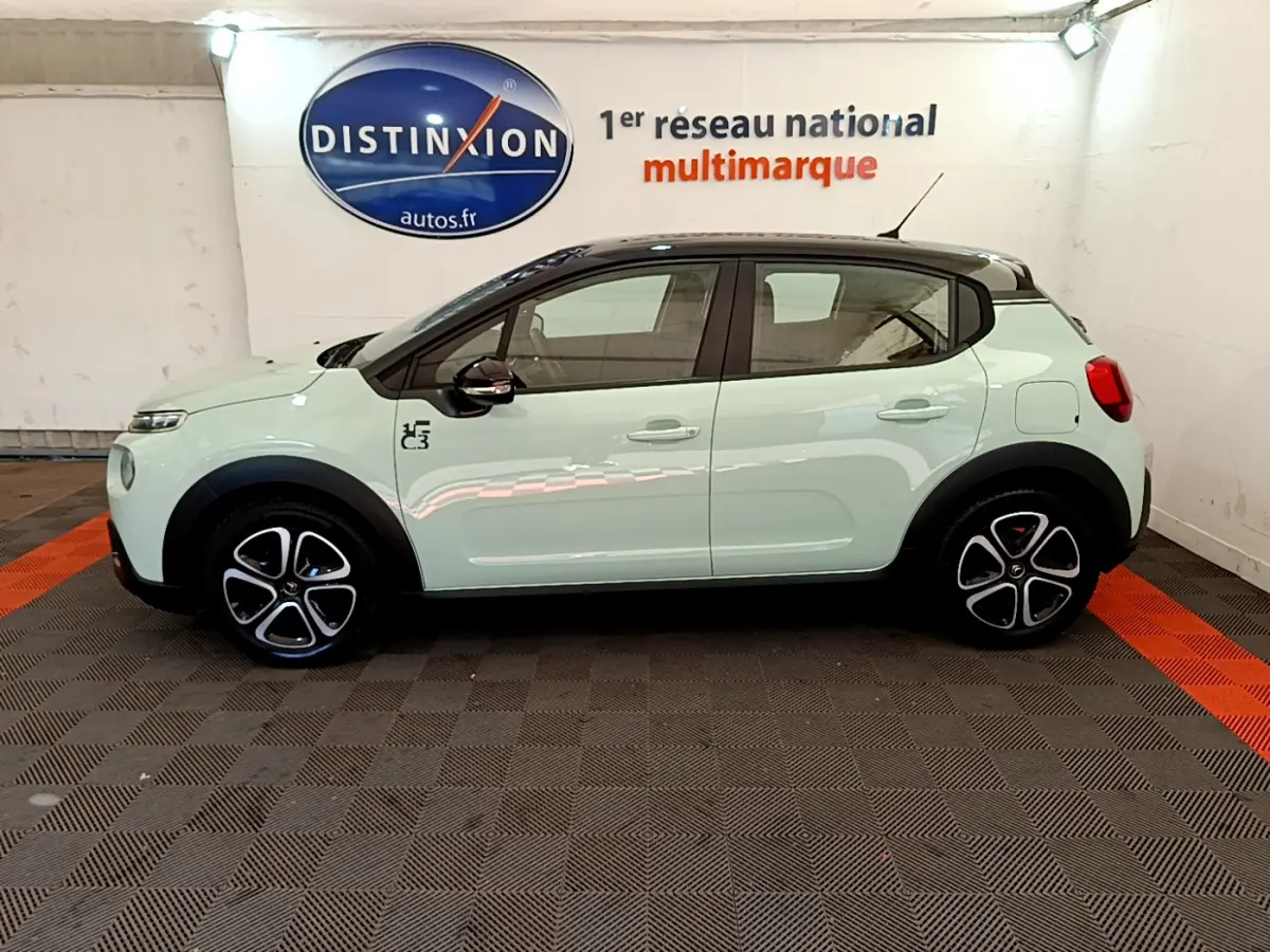 Profil latéral gauche d'une Citroën C3 PureTech 82 vert clair avec toit noir et jantes distinctives en concession.