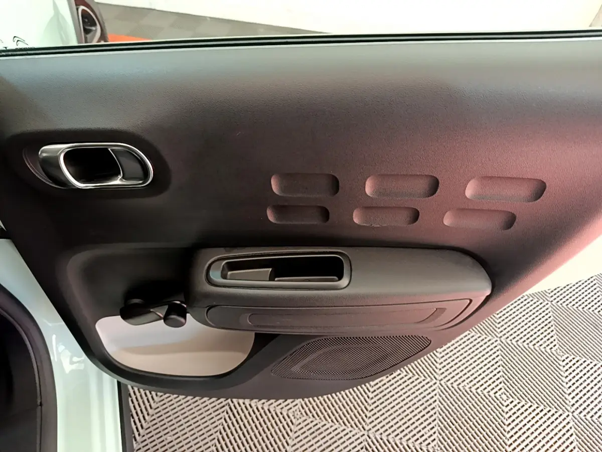 Vue rapprochée de la porte intérieure côté gauche de la Citroën C3 PureTech 82 verte avec poignée et commande de vitre manuelle.