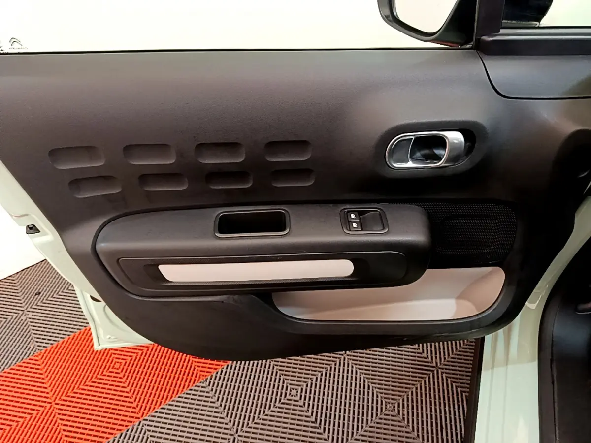 Intérieur côté gauche de la porte avant d'une Citroën C3 vert clair, avec poignée argentée et commandes de vitres.
