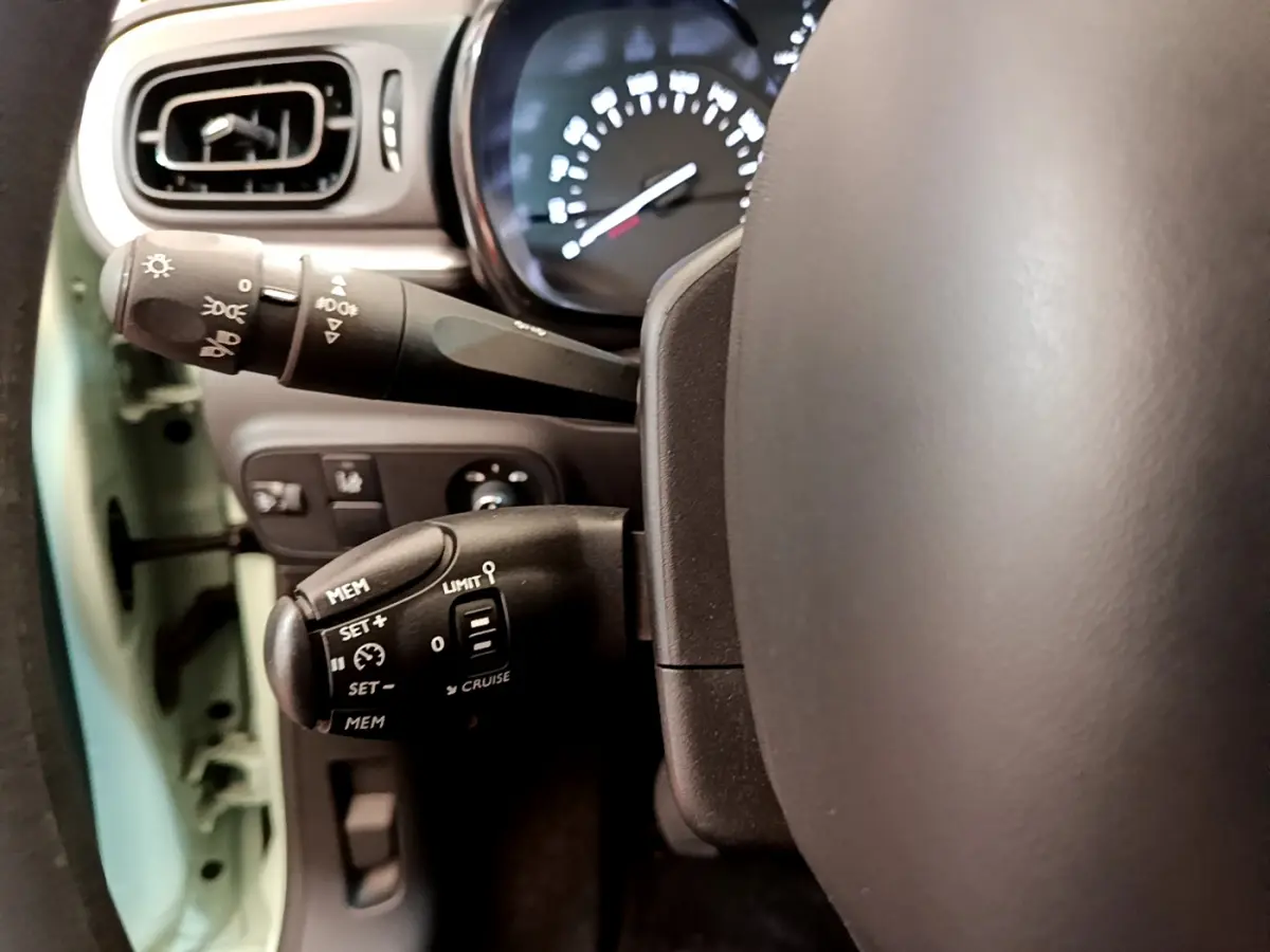 Gros plan sur la commande de régulateur de vitesse et le commodo d’éclairage dans une Citroën C3 vert 2019.