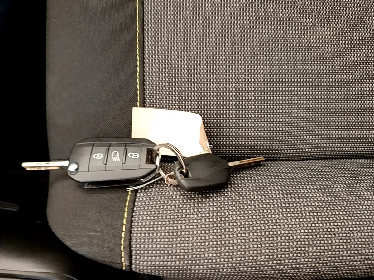 Clé de voiture Citroën C3 PureTech posée sur siège tissu gris avec surpiqûres vertes, vue rapprochée intérieure.