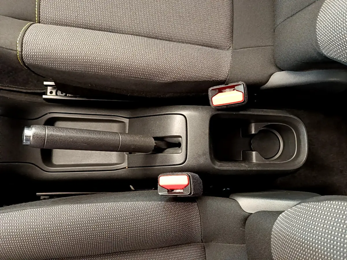 Vue plongeante sur la console centrale noire avec frein à main et ceintures rouges entre les sièges tissu gris de la Citroën C3.