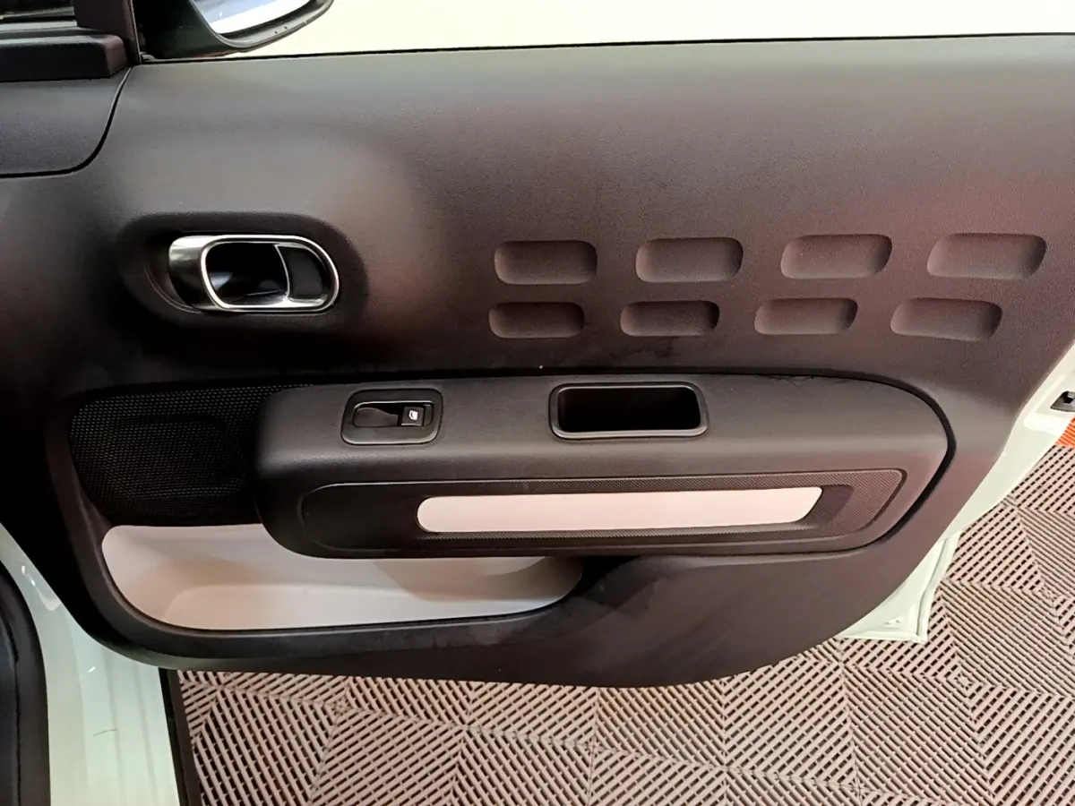 Gros plan sur la porte côté gauche vert clair de la Citroën C3 avec poignée chromée et bouton de commande de vitre.