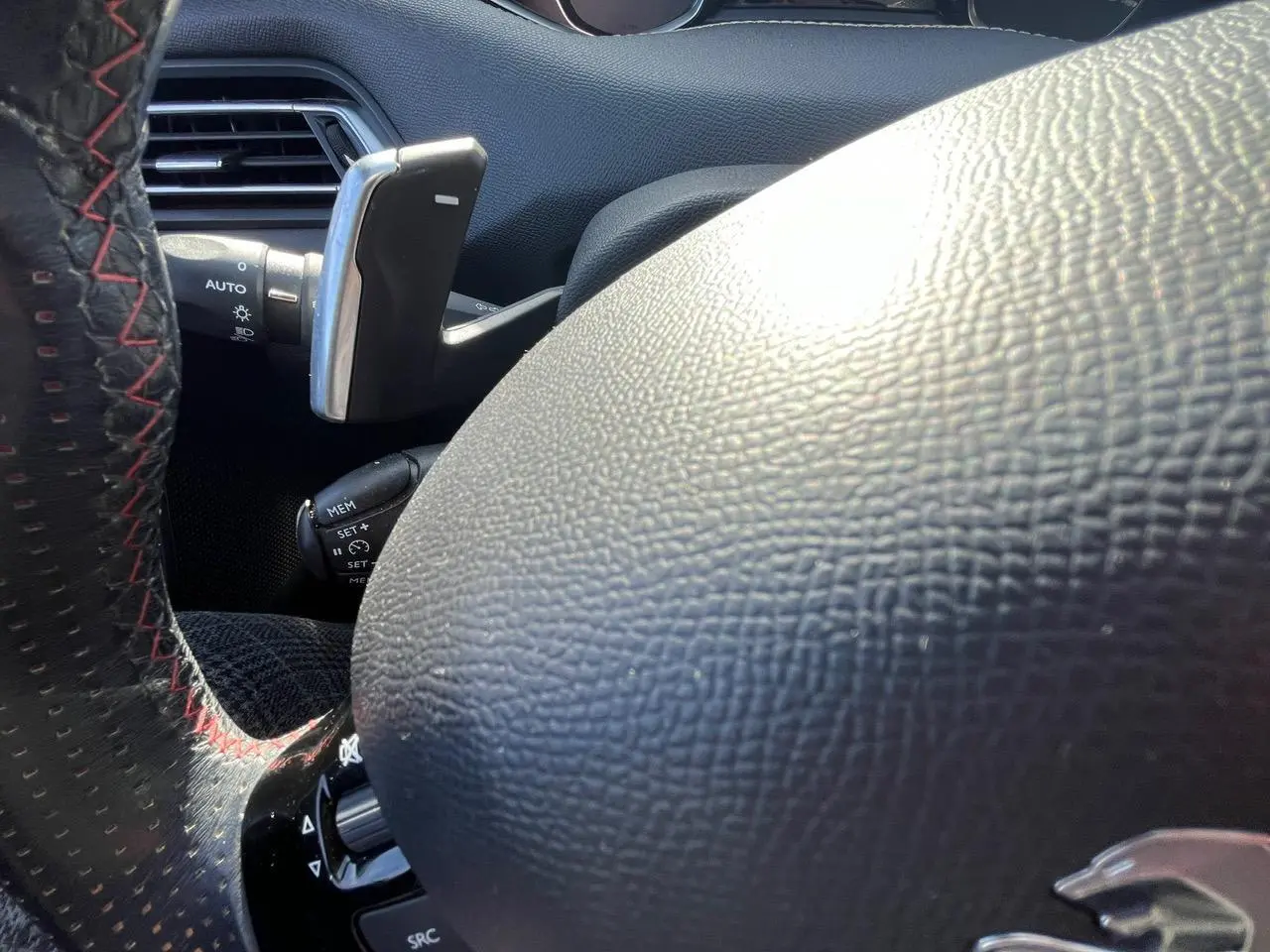 Gros plan sur le volant noir à surpiqûres rouges de la Peugeot 308 SW GT Line, mettant en valeur la commande au volant.