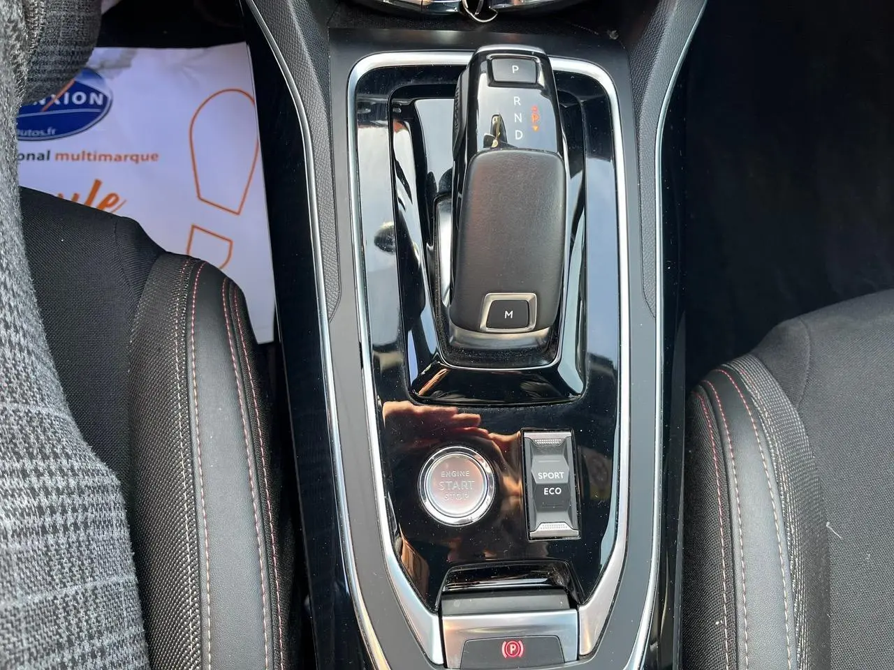 Vue plongeante sur la console centrale noire brillante de la Peugeot 308 SW GT Line, avec levier de vitesse auto et bouton start/stop.