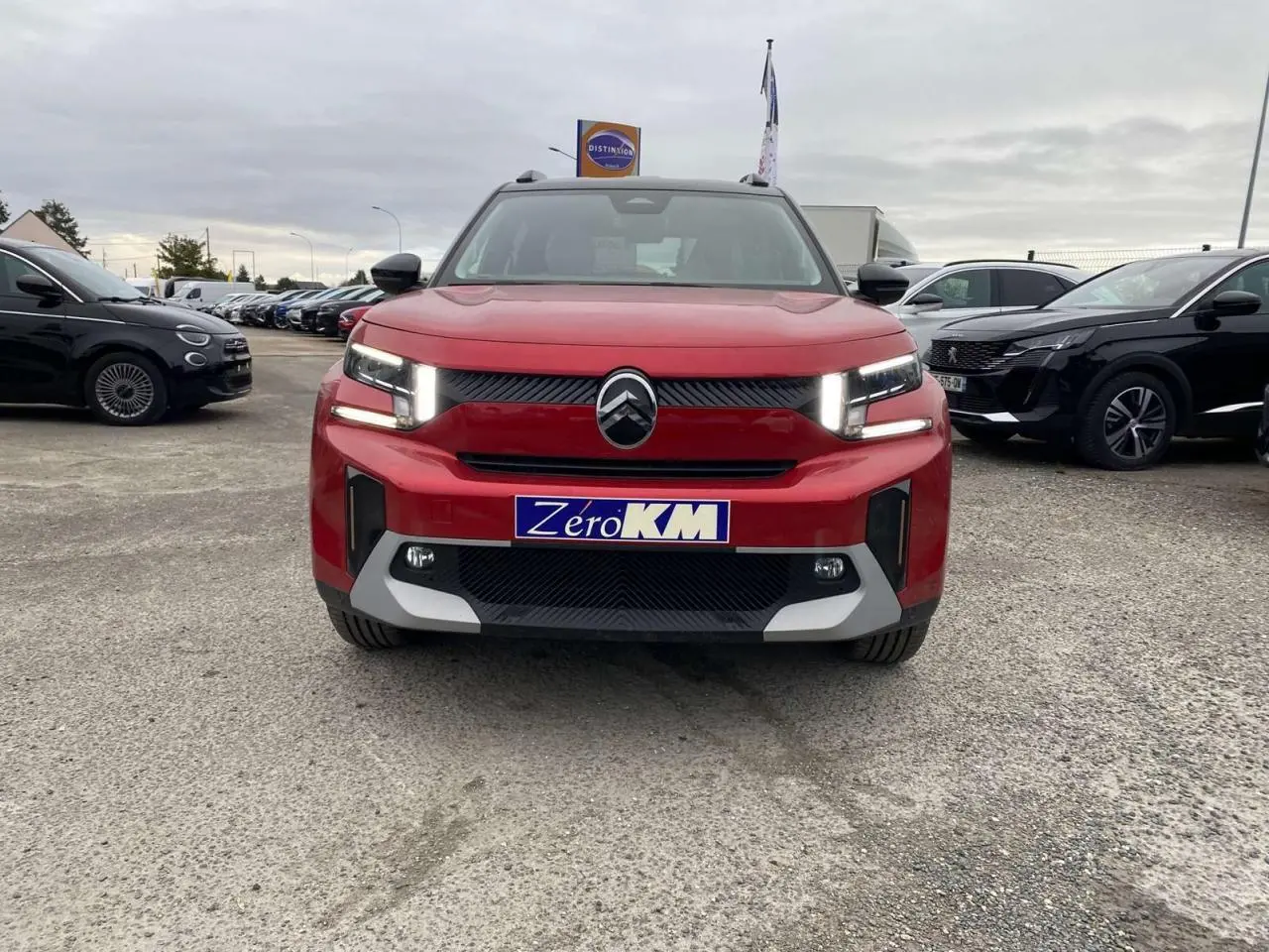 Vue frontale d'un Citroën C3 Aircross rouge Elixir avec toit noir, feux LED allumés sur parking extérieur.