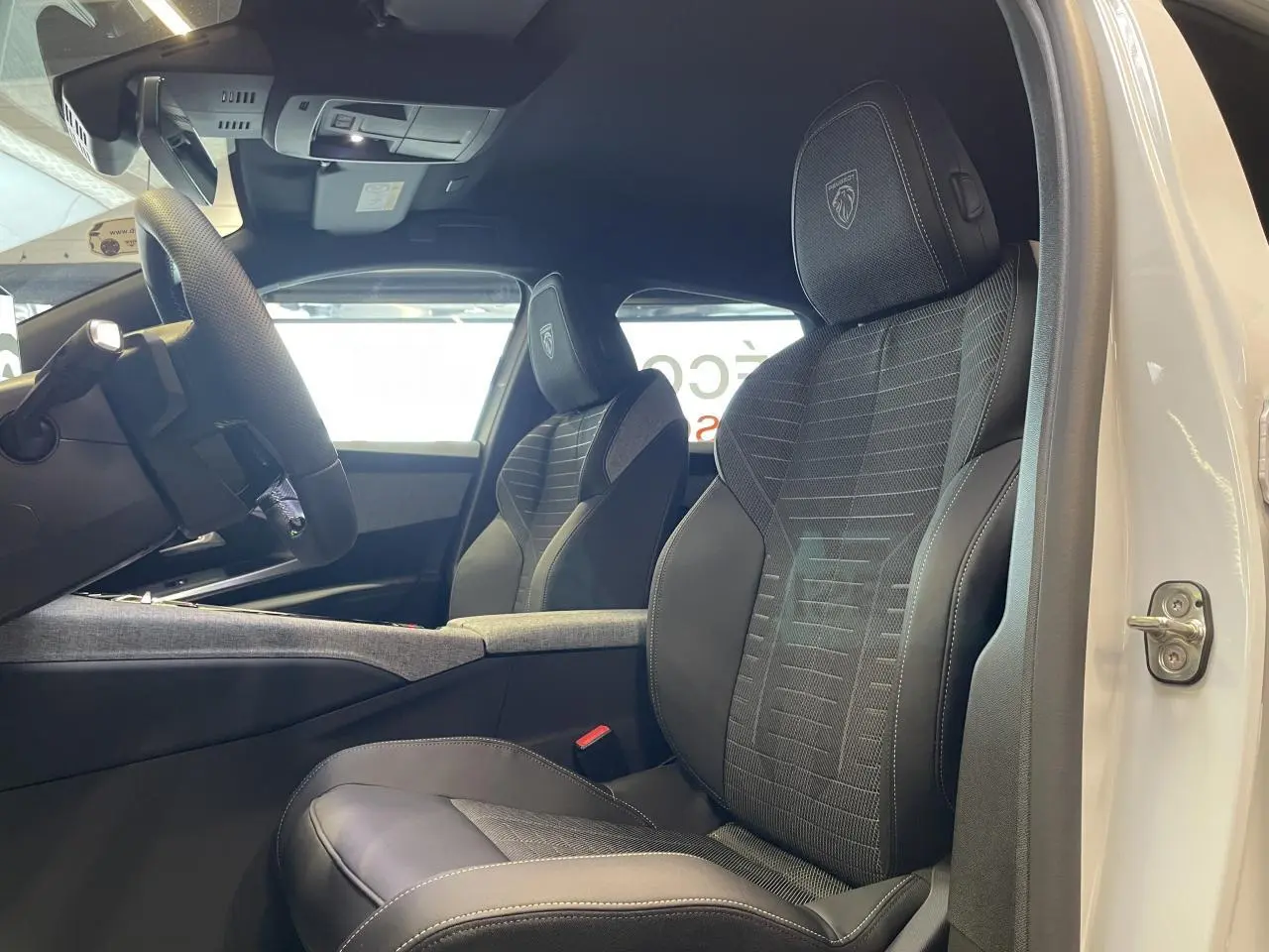 Vue intérieure côté conducteur du Peugeot 3008 blanc Okenite, sièges sport noirs avec logo Peugeot brodé sur appuie-tête.