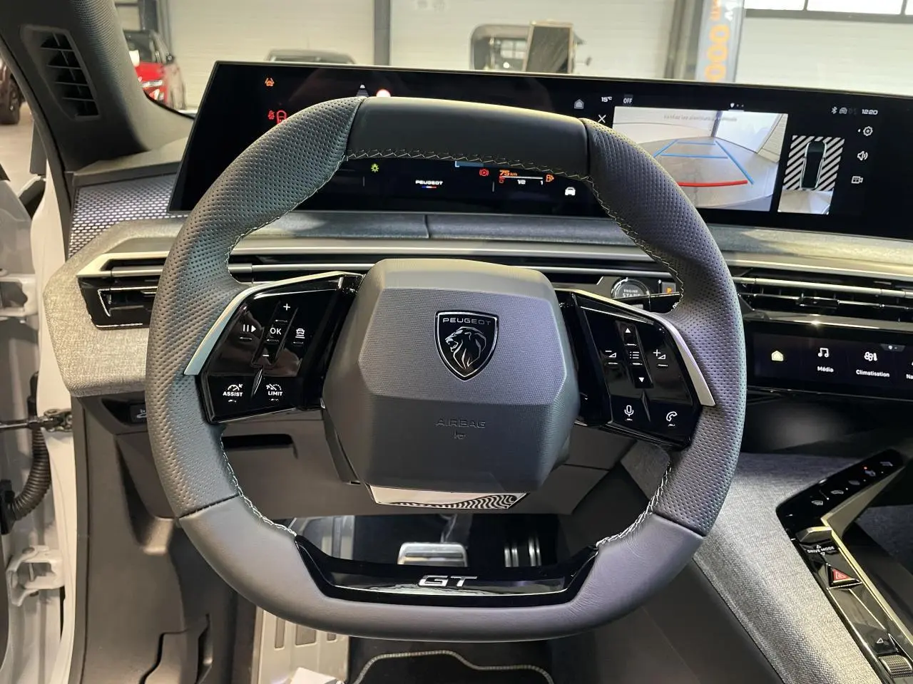 Vue rapprochée du volant cuir perforé avec badge GT du Peugeot 3008 Hybrid blanc, tableau de bord numérique en arrière-plan.