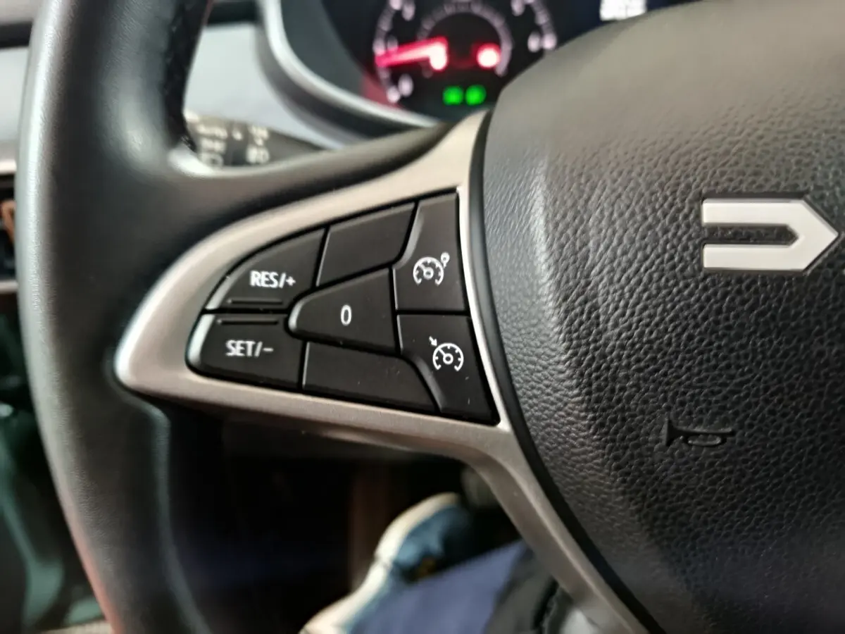 Gros plan sur les commandes de régulateur de vitesse à gauche du volant noir de la Dacia Sandero Extreme+ TCe 110 2024.