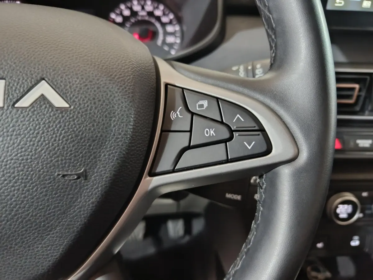 Gros plan sur le volant cuir noir de la Dacia Sandero 2024 avec commandes multifonctions et tableau de bord en arrière-plan.