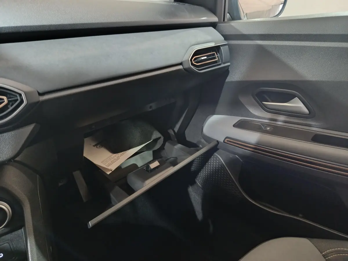 Vue intérieure côté passager de la Dacia Sandero Extreme+ 2024, tableau de bord noir avec boîte à gants ouverte.