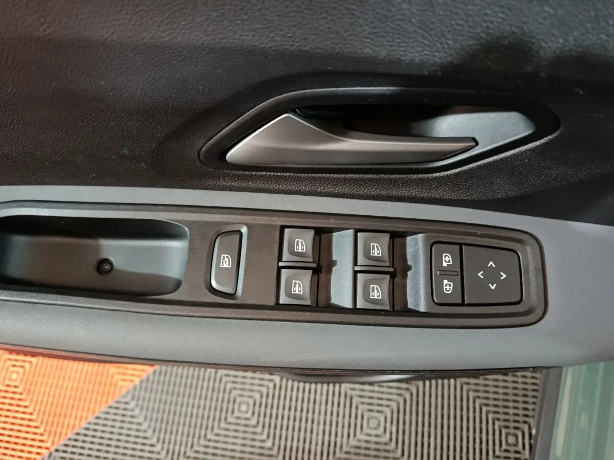 Gros plan sur la commande des vitres et rétroviseurs côté conducteur d'une Dacia Sandero vert 2024.