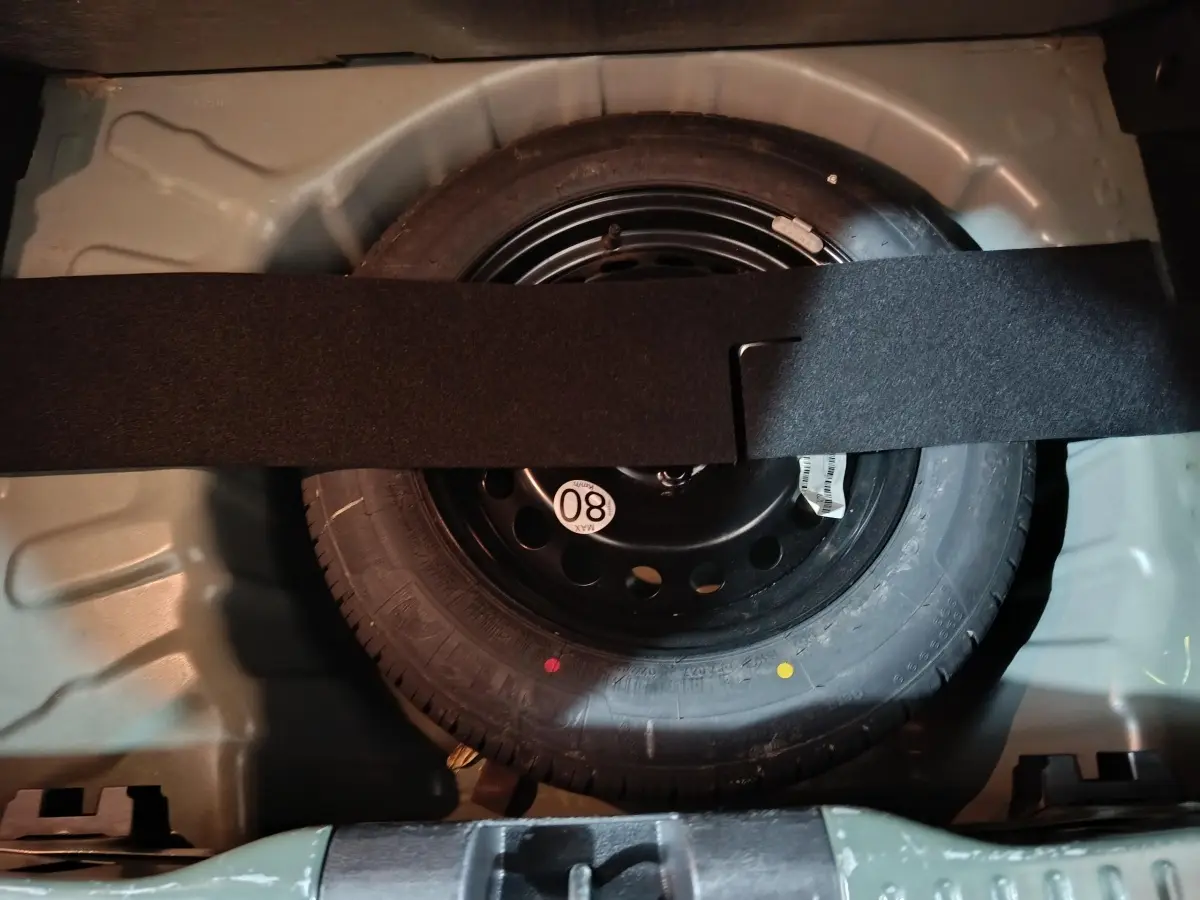 Vue rapprochée de la roue de secours galette noire dans le coffre vert de la Dacia Sandero Extreme+ TCe 110 2024.