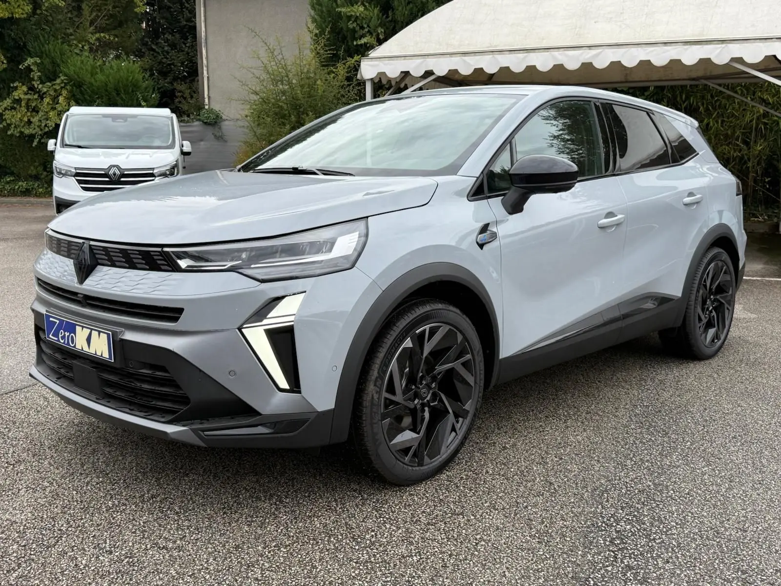 Vue 3/4 avant d’un Renault Symbioz gris rafale avec jantes noires et feux LED distinctifs, stationné sur un parking.