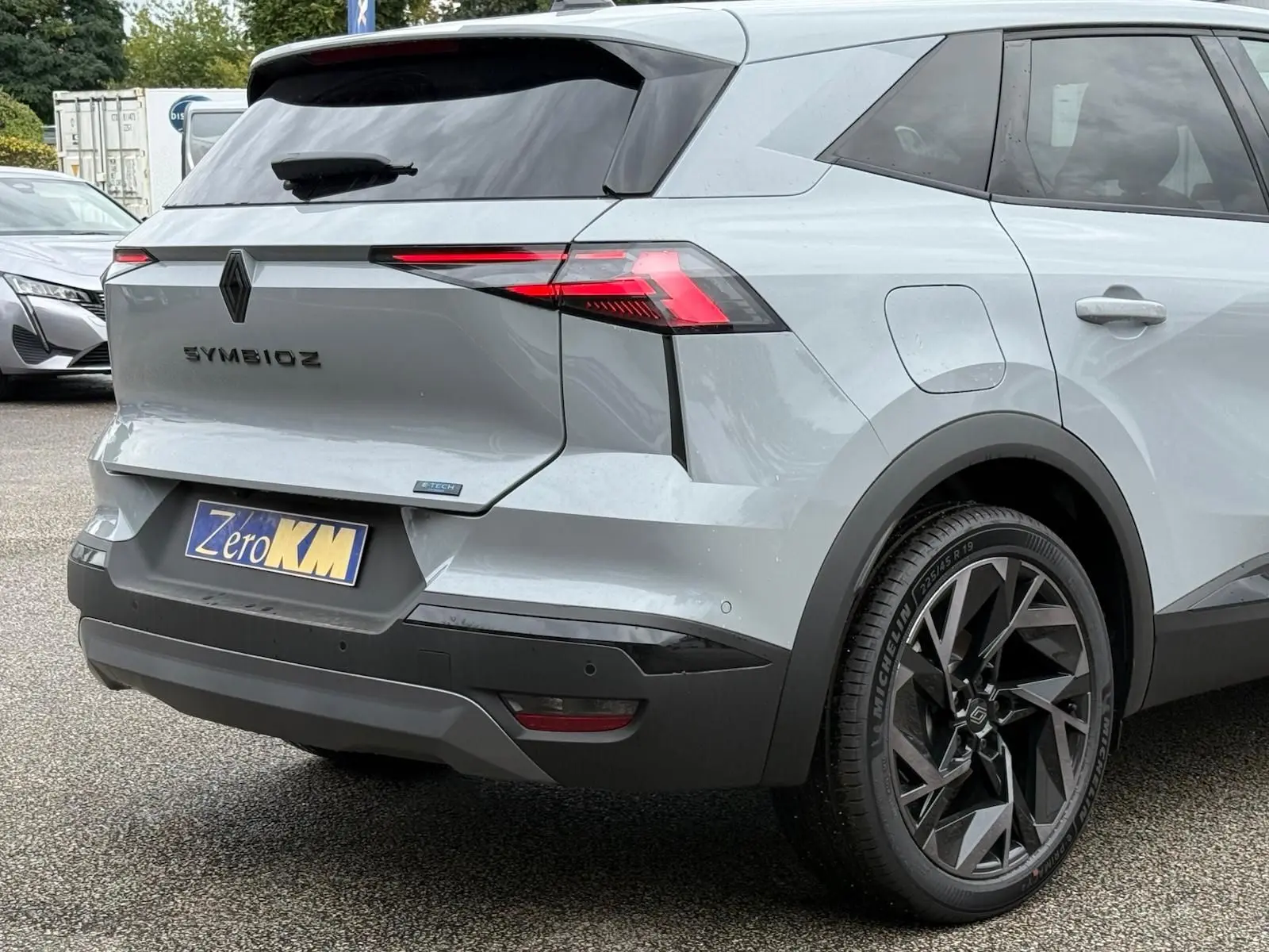 Vue 3/4 arrière droite du Renault Symbioz gris Rafale, mettant en valeur ses feux LED et ses jantes noires au design géométrique.