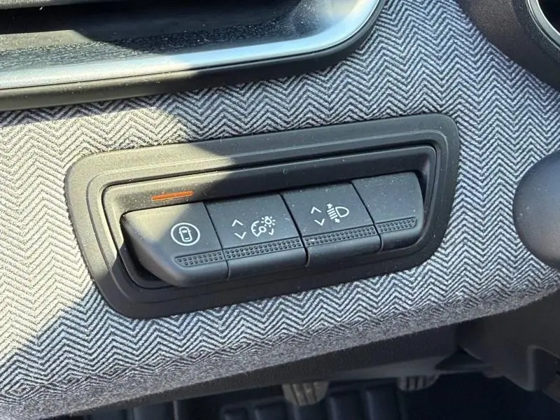 Gros plan sur les commandes de réglage des phares et du tableau de bord, avec tissu gris à motif chevron dans une Renault Clio 2025.
