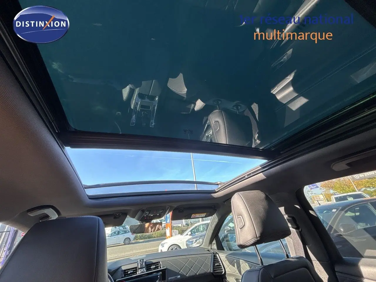 Vue intérieure du toit panoramique ouvert du DS7 Crossback E-TENSE 2021 en cuir noir, avec lumière naturelle et ciel visible.