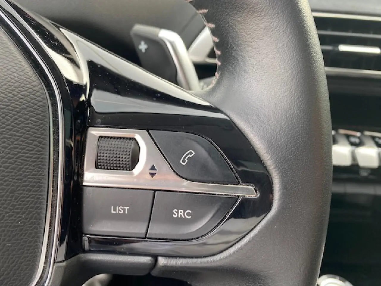 Gros plan sur les commandes gauche du volant cuir noir du Peugeot 3008 gris platinium 2021 finition Allure Pack.