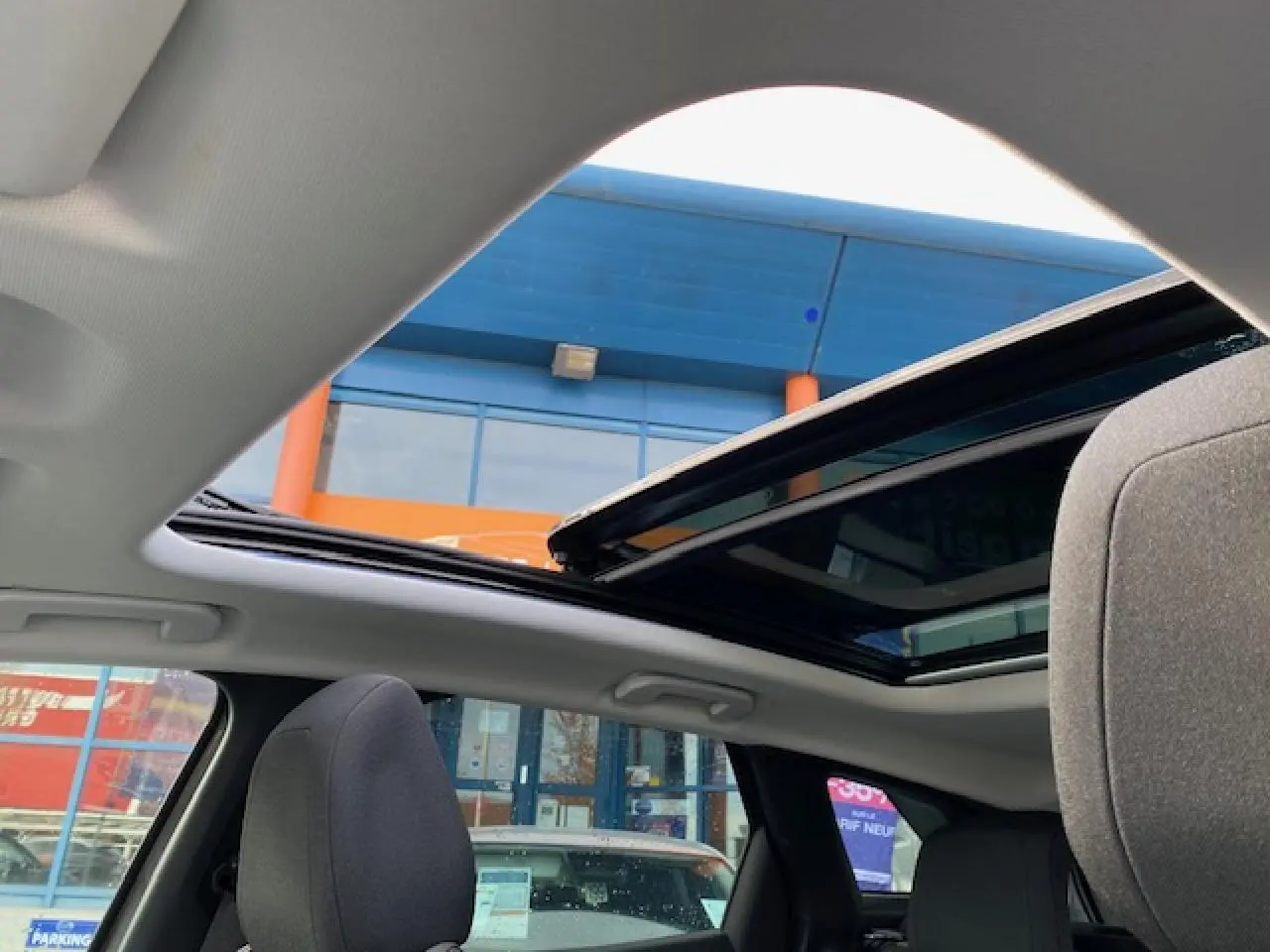 Vue intérieure du toit ouvrant panoramique ouvert sur Peugeot 3008 gris platinium, avec sièges avant en tissu gris.