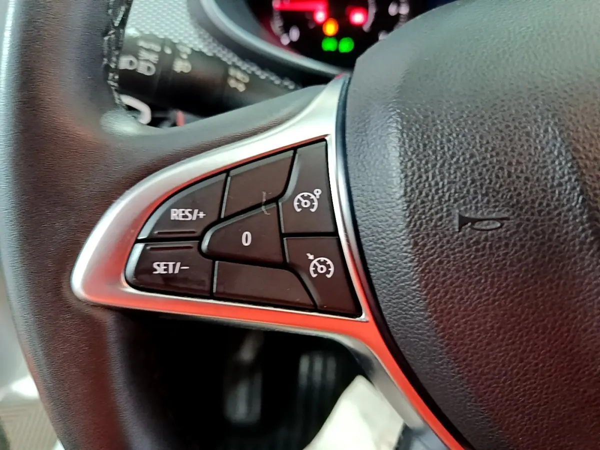 Gros plan sur le côté gauche du volant cuir synthétique noir du Dacia Sandero blanc, avec commandes de régulateur de vitesse.