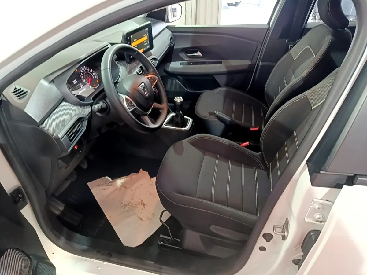 Vue intérieure côté conducteur d'une Dacia Sandero blanc 2022, volant cuir multifonctions et sièges tissu noirs.