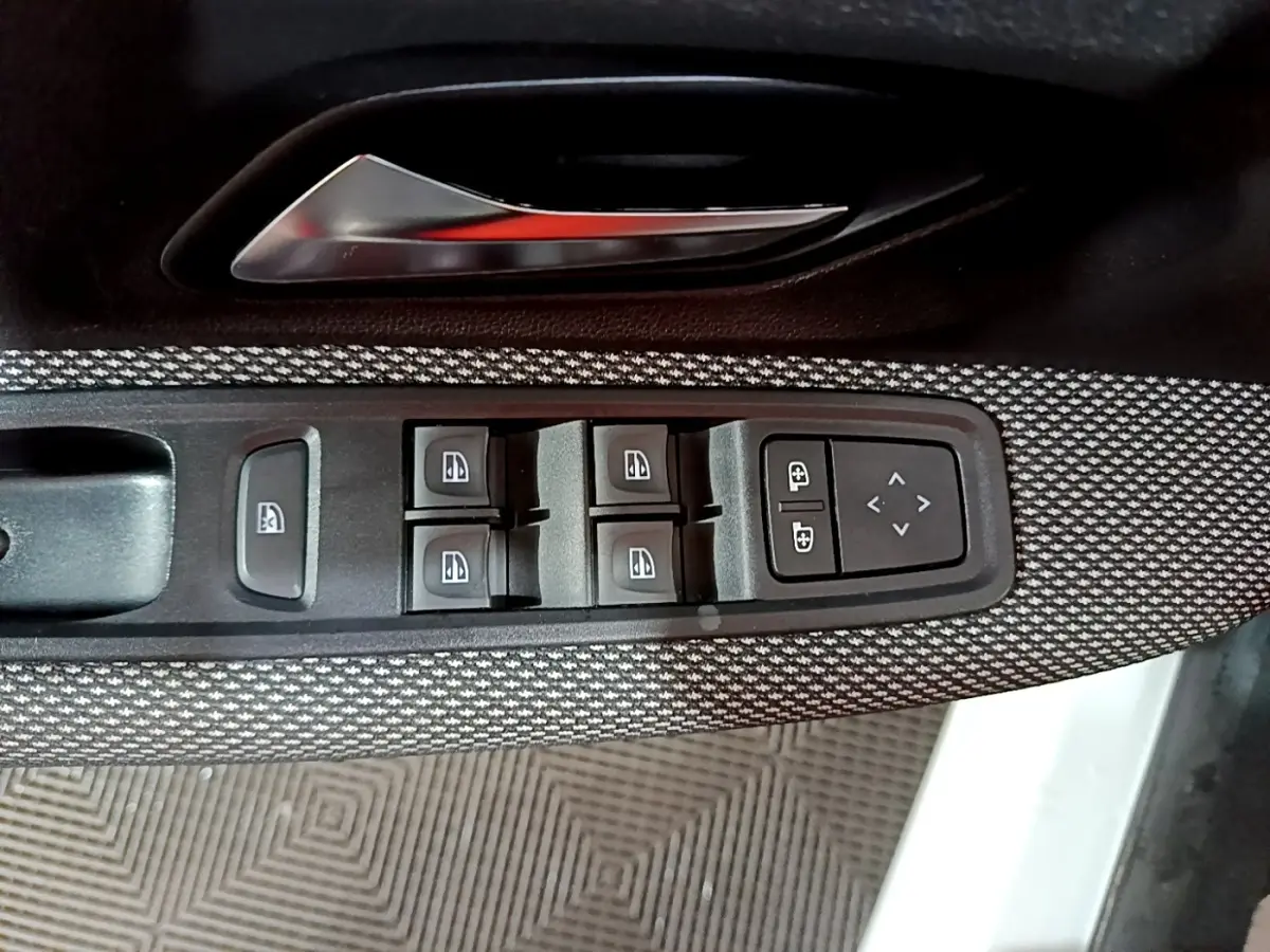 Gros plan sur la commande des vitres électriques et réglages des rétroviseurs côté conducteur d'une Dacia Sandero blanche.