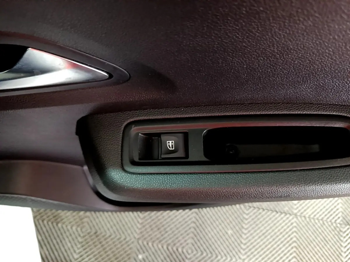 Gros plan sur le bouton de commande de la vitre électrique sur la porte intérieure noire d'une Dacia Sandero blanche.