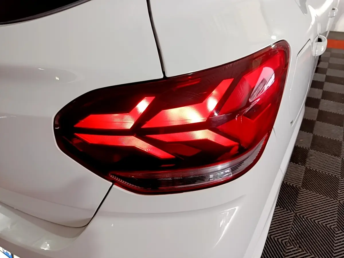 Gros plan sur le feu arrière droit rouge d'une Dacia Sandero blanche, vue partielle du coffre et de la portière arrière.