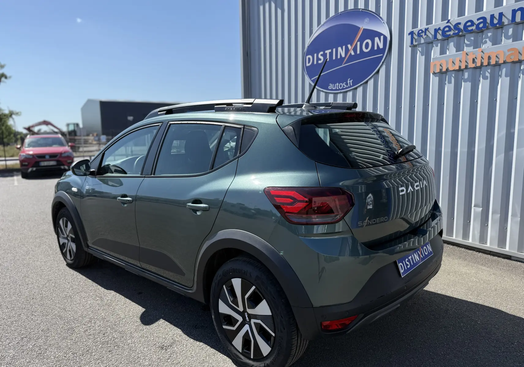 Vue 3/4 arrière droite d'une Dacia Sandero Stepway 2025 vert cèdre avec jantes distinctives et barres de toit noires.